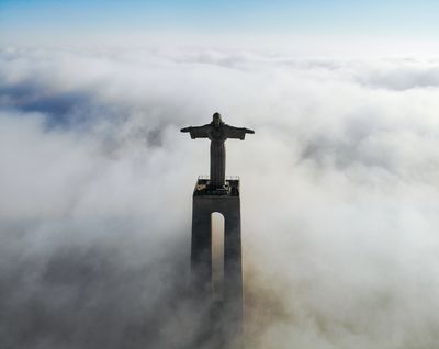 Statue of Jesus on pedestal above the clouds.