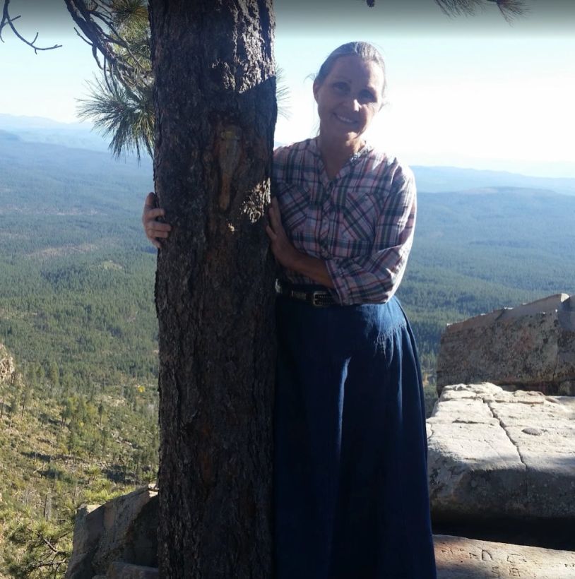 Woman smiling and leaning on a tree in a mountainous area.