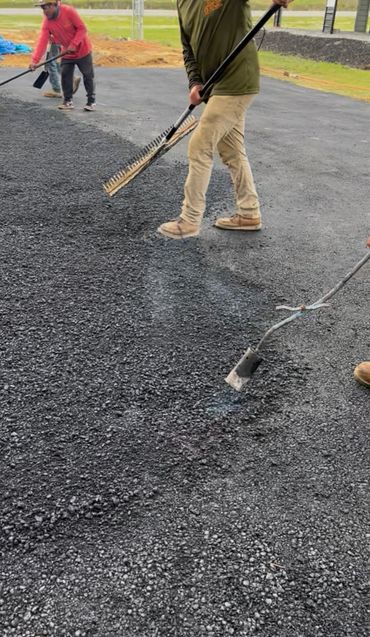 Workers spreading and leveling asphalt on a road surface.
