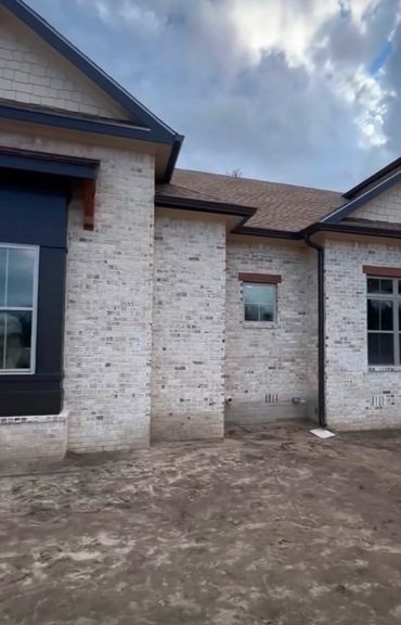 Newly built light brick house exterior with large windows and cloudy sky.