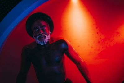 Elderly man with closed eyes illuminated by red and blue light.
