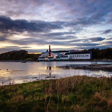 Lacavulin distillery by a calm waterfront at sunset with dramatic clouds.