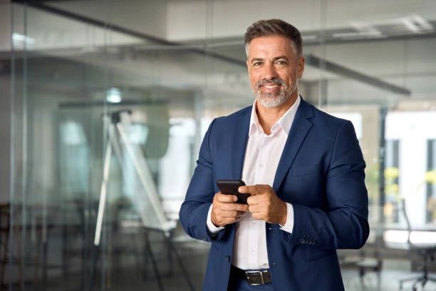 Confident businessman in a blue suit using a smartphone in an office.