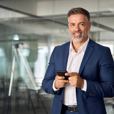 Confident businessman in a blue suit using a smartphone in an office.
