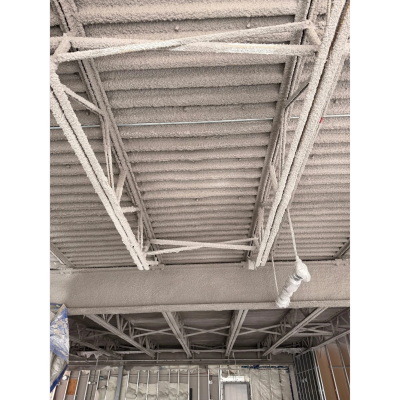 Professional cementitious fireproofing being spray-applied to structural steel and a metal deck, cre