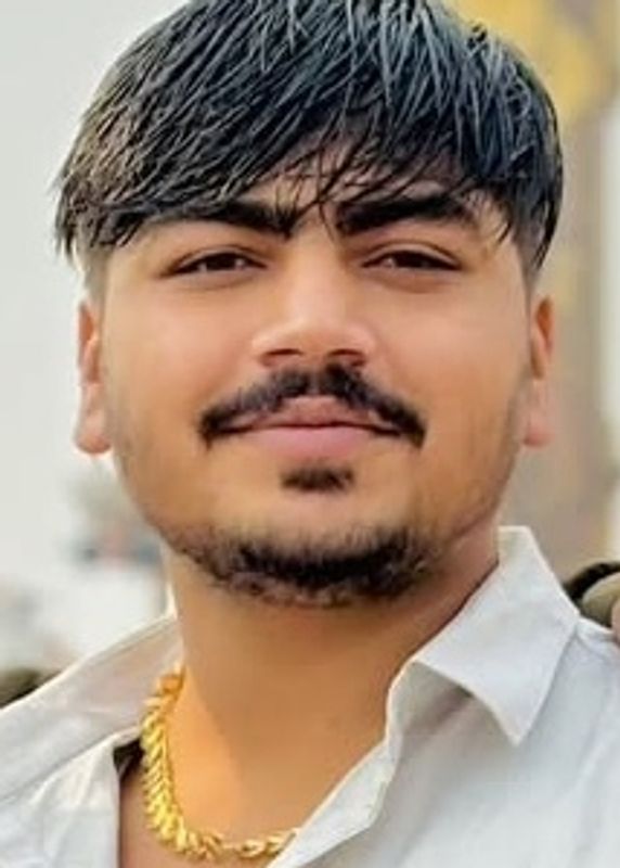 Young man with a hairstyle and gold chain smiling at the camera.