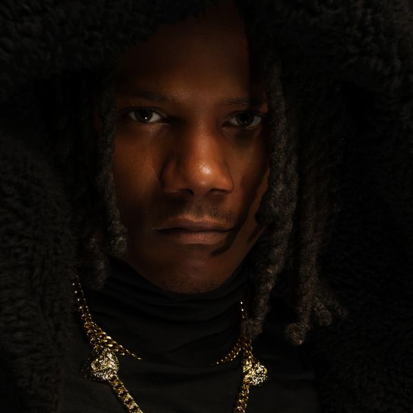 Close-up portrait of a serious man with dreadlocks and gold chains.