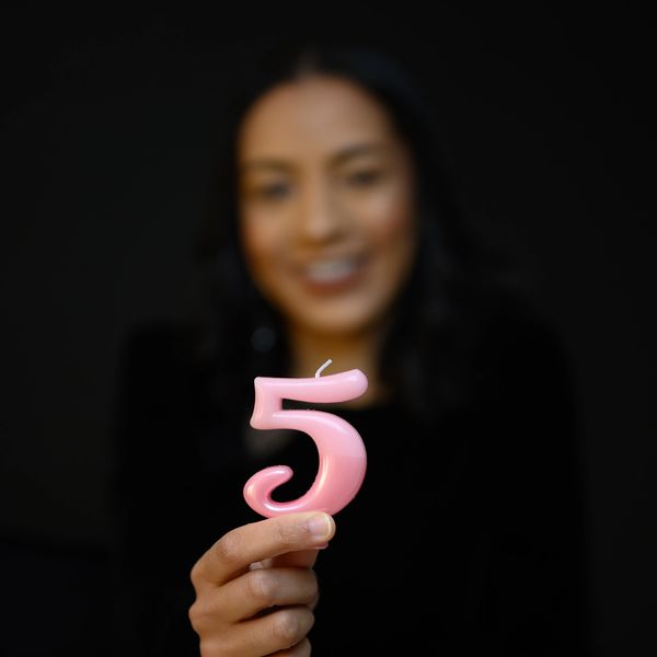 Person holding a pink number 5 candle in focus, face blurred.