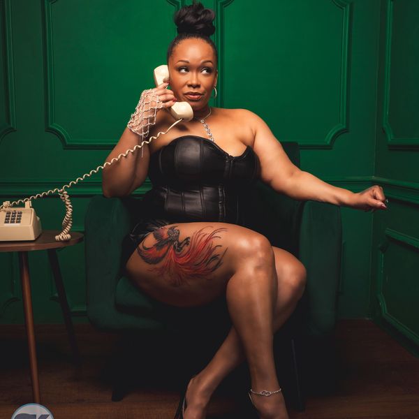 Woman in black corset dress with leg tattoo talking on a vintage phone.
