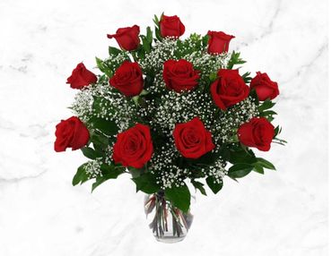 A bouquet of red roses with white baby's breath in a clear vase.