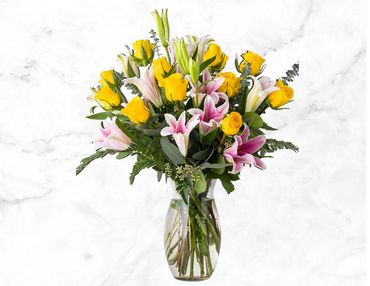 A vibrant bouquet of yellow roses and pink lilies in a clear glass vase.