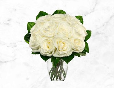 Elegant bouquet of white roses in a clear glass vase with green leaves.