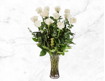 Elegant bouquet of white roses in a glass vase with green foliage.
