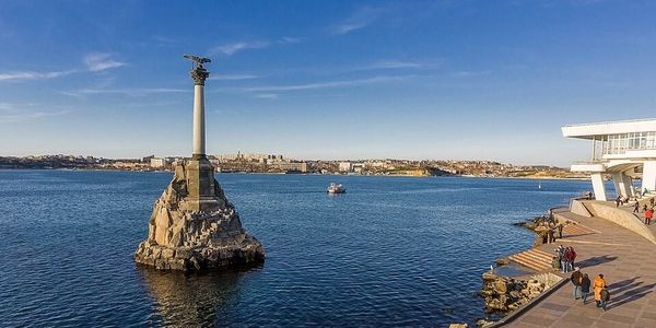 Monument on a rock in the sea near a coastal walkway with people.