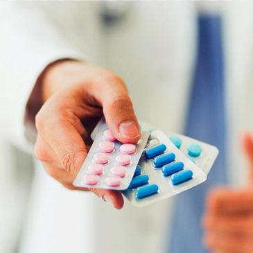 A hand holding blister packs of pink and blue pills.
