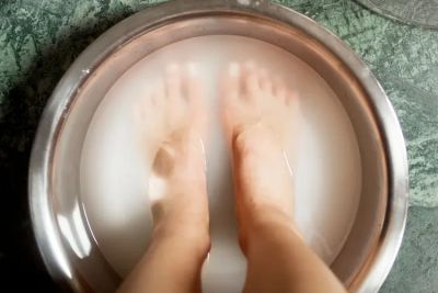 Feet soaking in a milky white liquid in a metal basin.