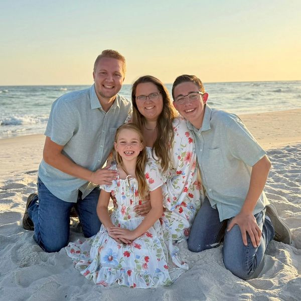 Happy family of four posing on the beach at sunset.
