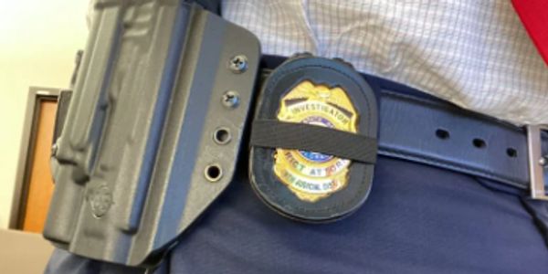 Close-up of a police officer's duty belt with a holstered firearm and badge.