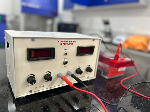 Close-up of a DC power supply unit with connected red and black wires.