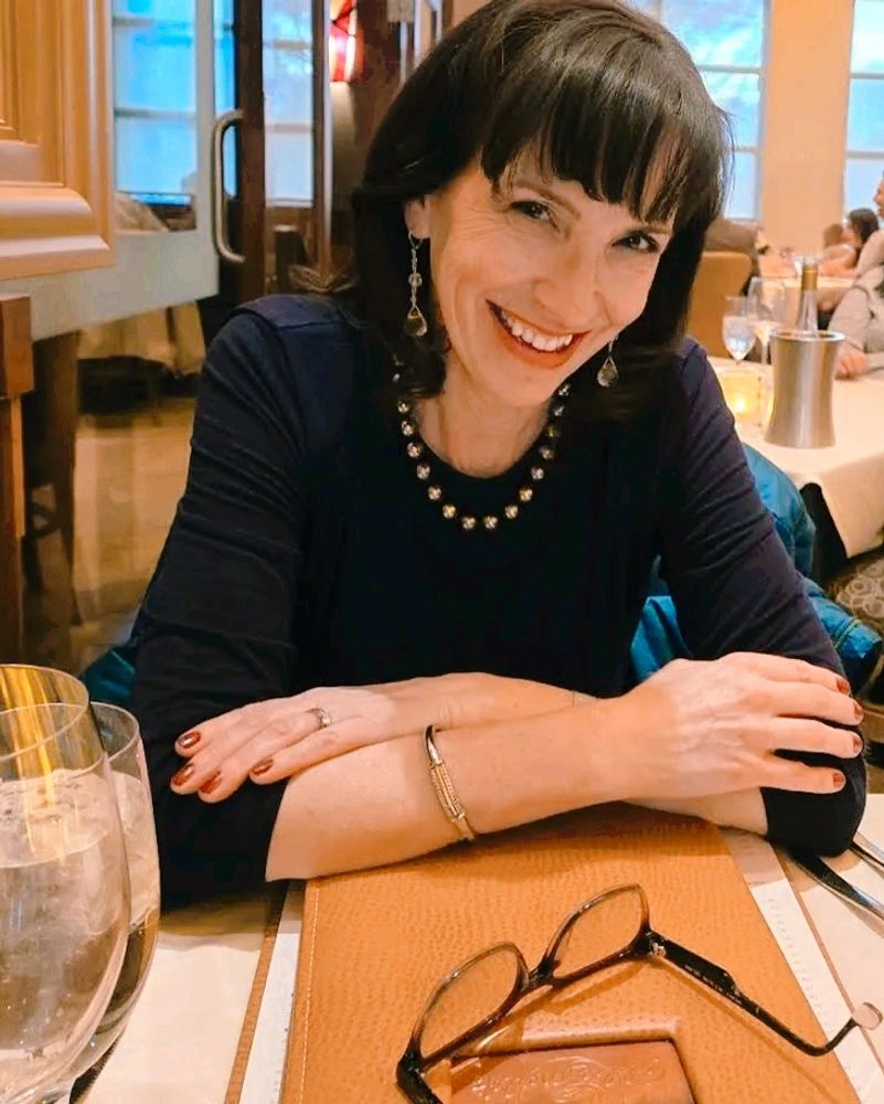 Smiling woman sitting at a restaurant table with glasses in front.