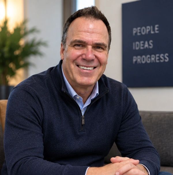 Man smiling, seated indoors with motivational sign behind.