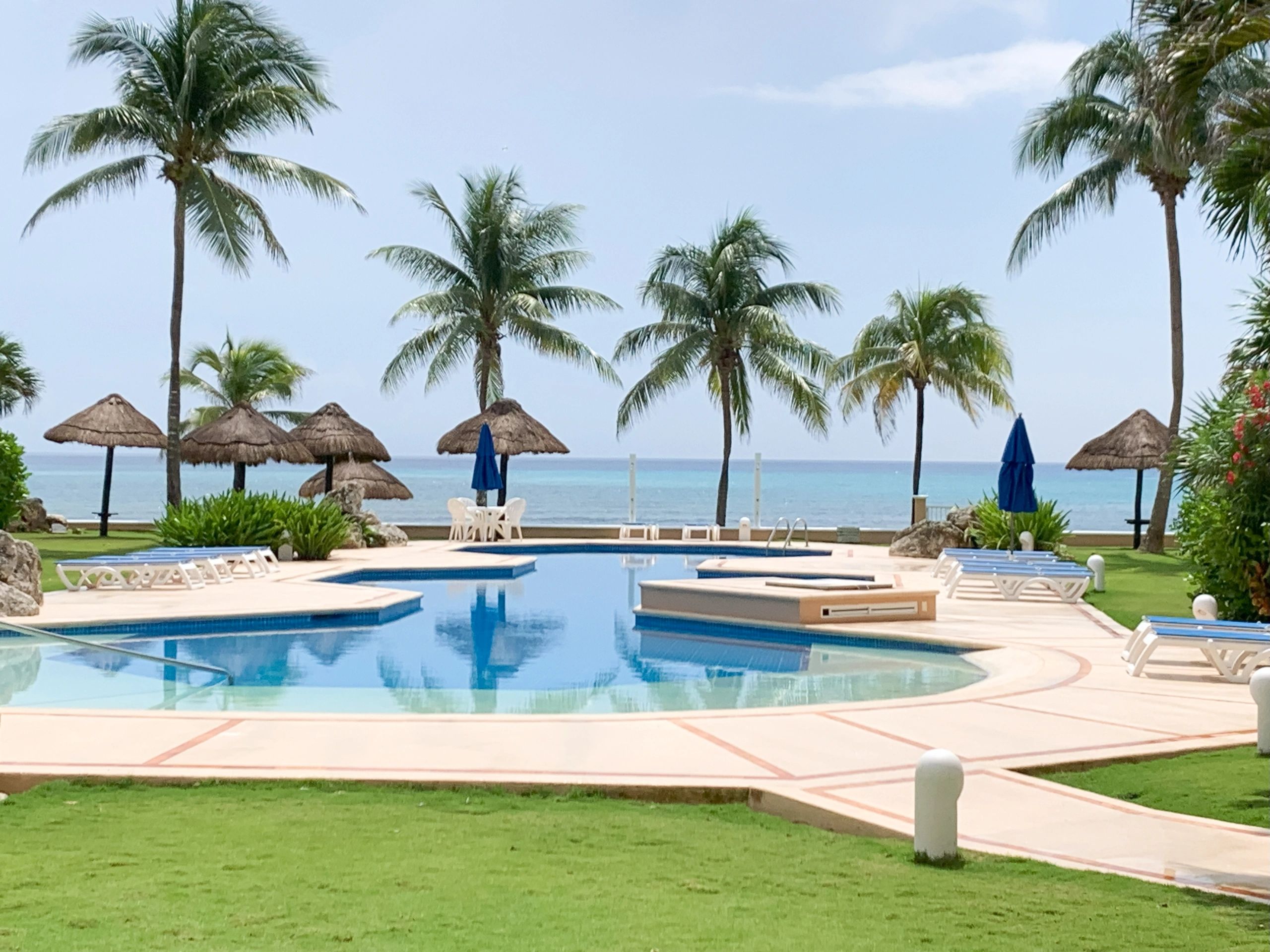 "Piscina frente al mar Caribe con palmeras y camastros en resort de lujo en Puerto Aventuras – Mayan Getaways"