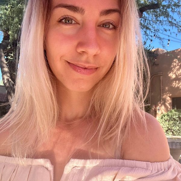 Young woman with blonde hair smiling outdoors in natural light.