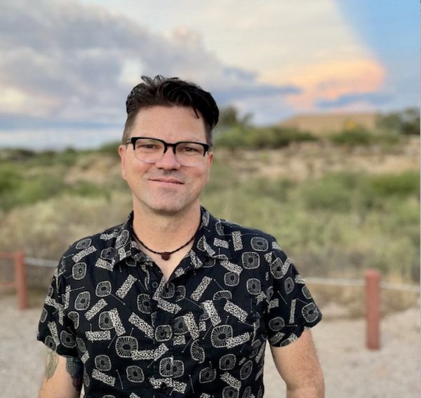 Man wearing glasses and patterned shirt outdoors.