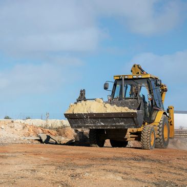 Yellow loader moving soil on a construction site under a clear sky.
