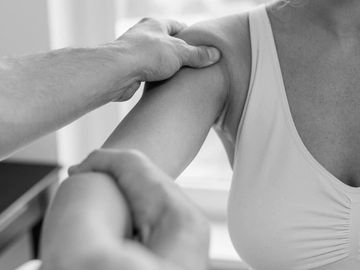 Physical therapist examining a woman's shoulder during therapy session.