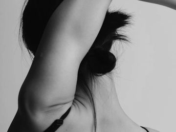 Black and white photo of a woman with her arm raised, showing her back and neck.