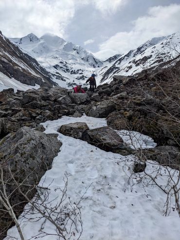 Two children climbing rocky, snowy terrain in a mountainous area.