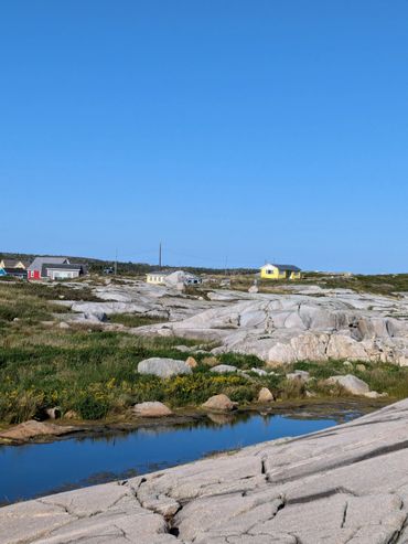 Coastal landscape with rocky terrain, small houses, and clear blue sky.