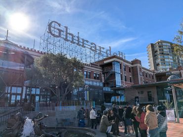 Crowd gathered outside the historic Ghirardelli building on a sunny day.