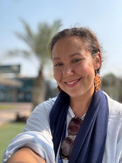 Smiling woman outdoors with palm tree background.