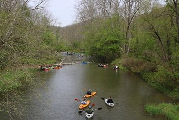 People kayaking on a calm river surrounded by trees in early spring.
