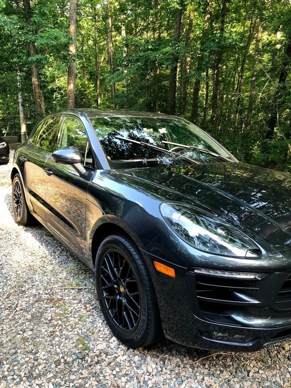 A sleek black Porsche SUV parked on a gravel path surrounded by trees.
