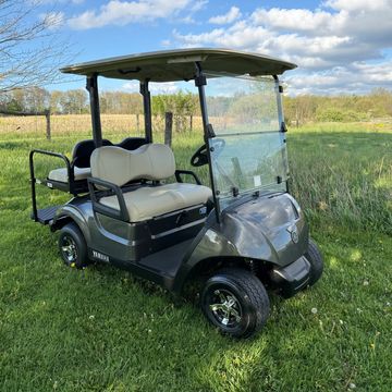 A black Yamaha golf cart parked on grass under a blue sky.