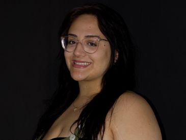 A woman with glasses smiling against a black background.
