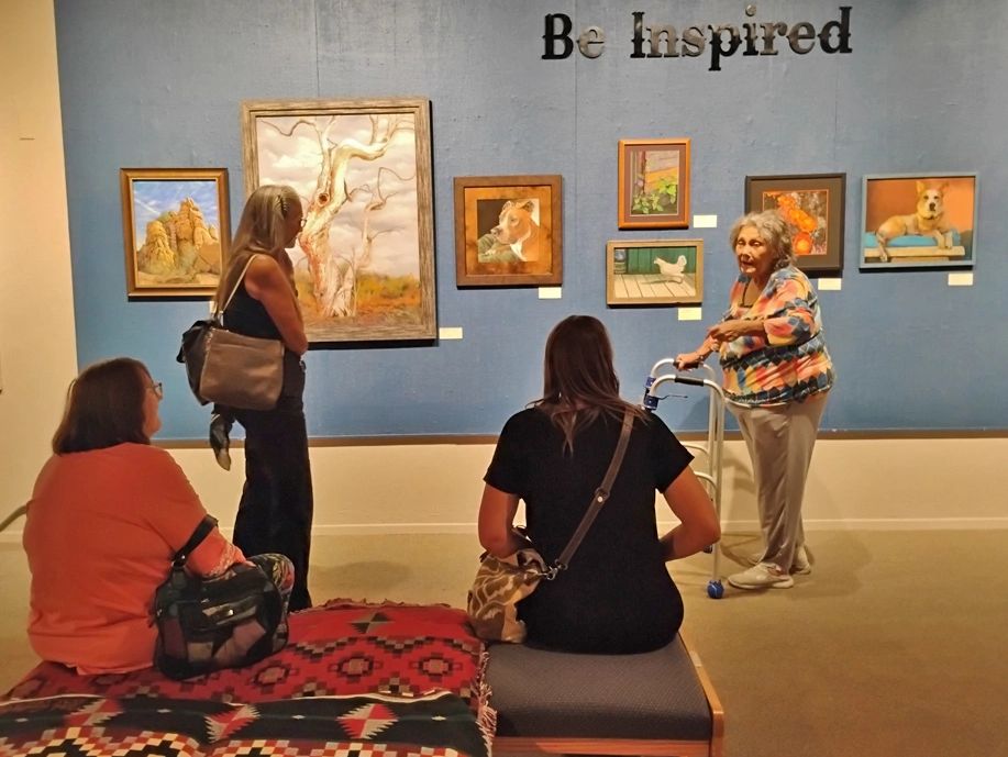 Be Inspired is written on the wall of paintings in a room with four participants in conversation.