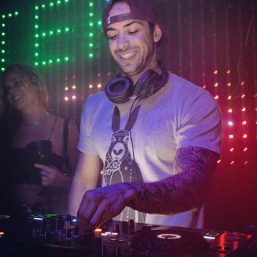 DJ mixing music with headphones around his neck and colorful lights.