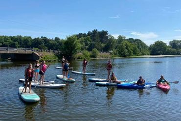 Group paddleboarding and kayaking on a calm river under a clear sky.