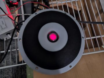 Top view of a round speaker with a red light in the center.