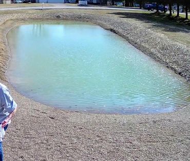 Small, man-made pond surrounded by gravel with a person partially visible on the left.