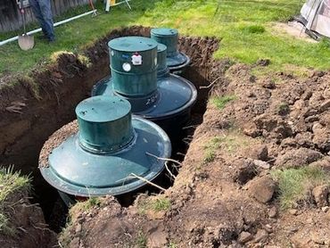 Three large green tanks partially buried in a dug trench outdoors.