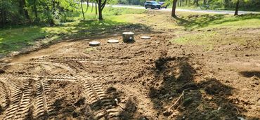 Freshly dug soil with tire tracks and circular concrete covers near a roadside.