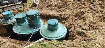 Large green septic tanks being installed in a dug-out earth trench.