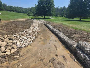 Construction site with rocky drainage channel in a green park area.
