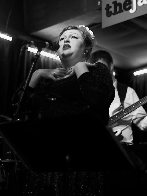A woman passionately singing on stage with a microphone in a dimly lit jazz club.