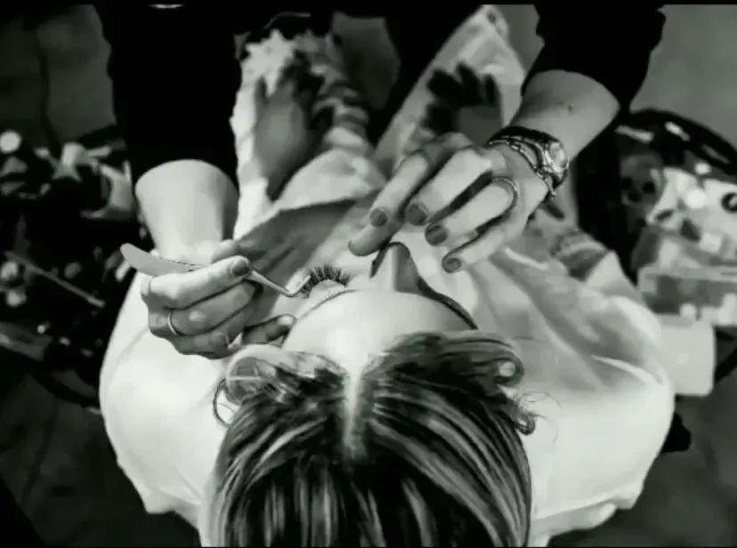 Applying false eyelashes to a woman lying down.